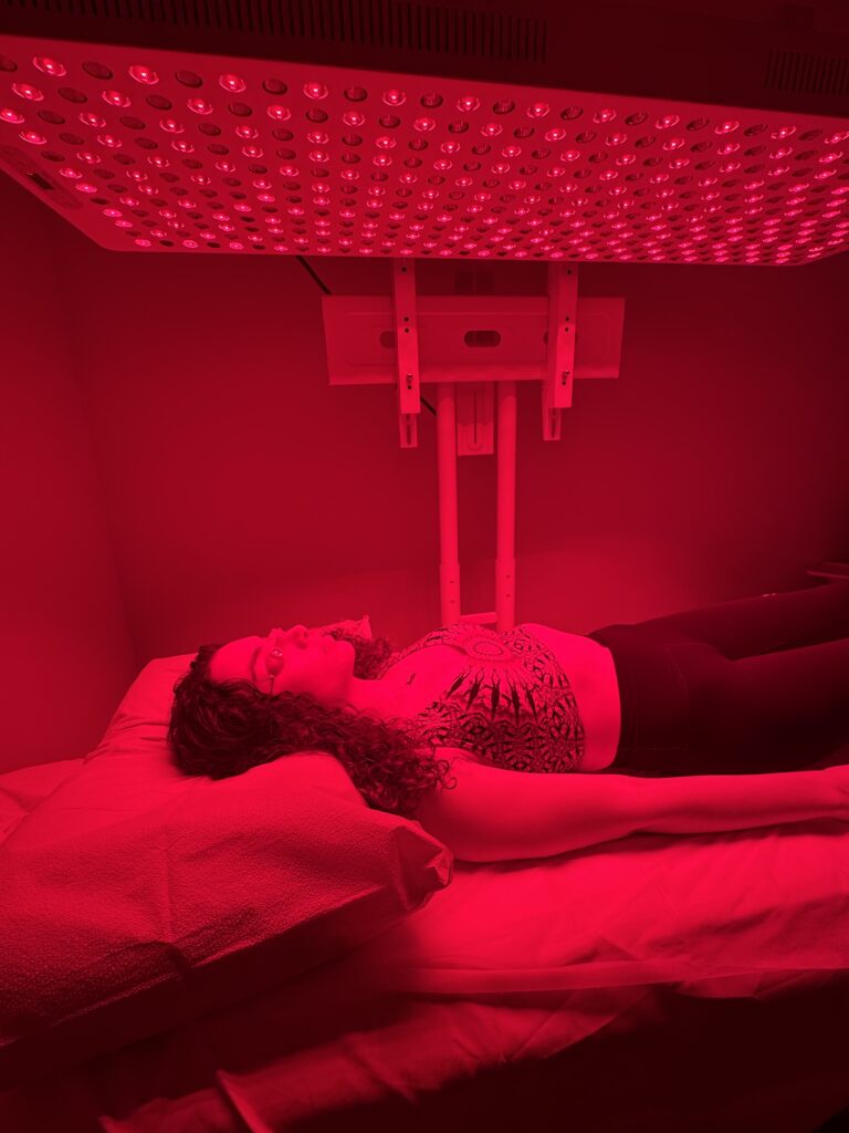 Person relaxing in a red light therapy booth for skin rejuvenation and cellular healing.
