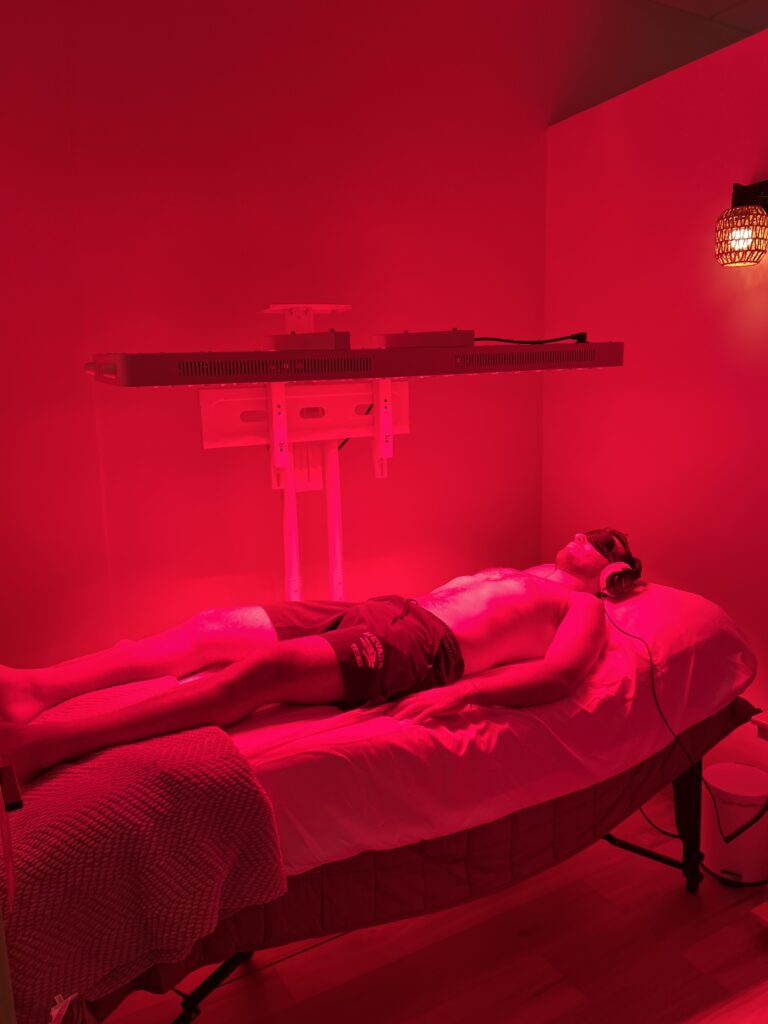 Client lying on a vibroacoustic bed, with red light therapy, during a sound frequency healing session.