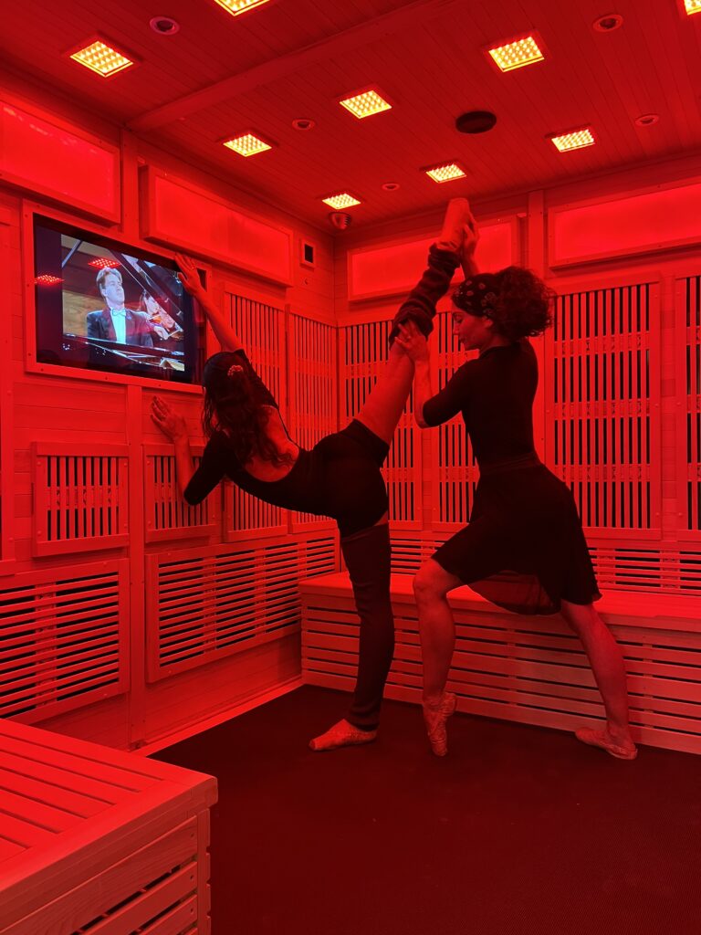 Two women stretching and working out inside the InfraRed Fit Room Sauna.